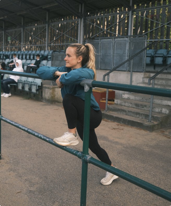 Tamara stretching on a railing at an athletics stadium