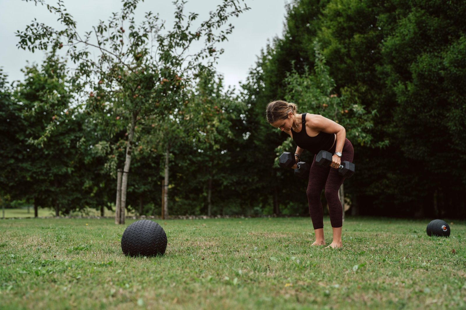 Tamara doing dumbbell rows on a lawn in front of trees
