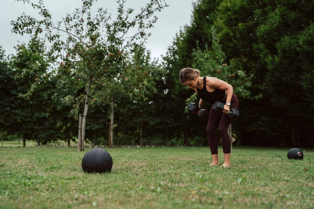 Tamara doing dumbbell rows on a lawn in front of trees