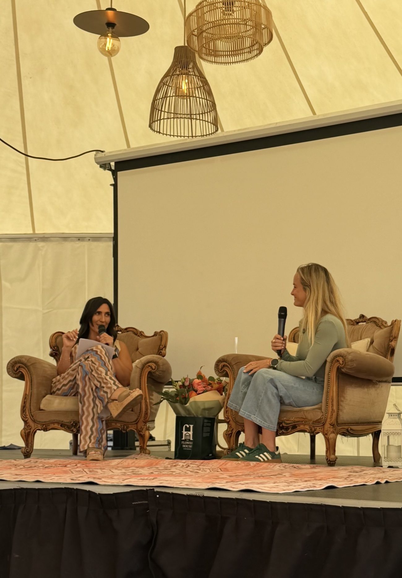 Tamara speaking on stage in a panel interview, seated in an armchair with a microphone
